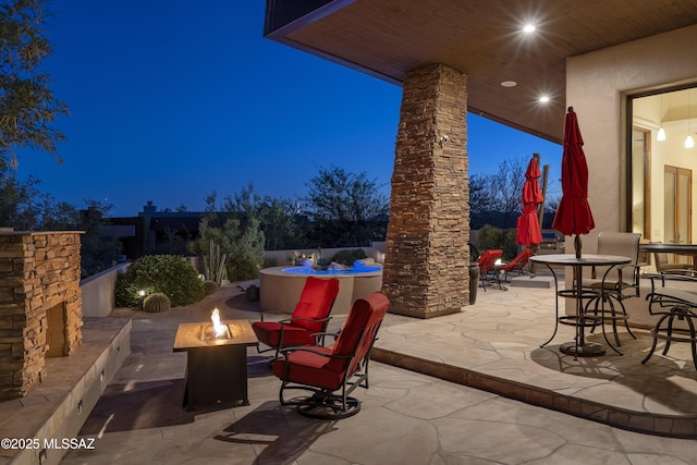patio at twilight featuring an outdoor stone fireplace and an outdoor fire pit