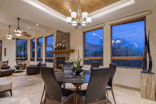 dining room with a stone fireplace, recessed lighting, tile patterned floors, a tray ceiling, and ceiling fan with notable chandelier
