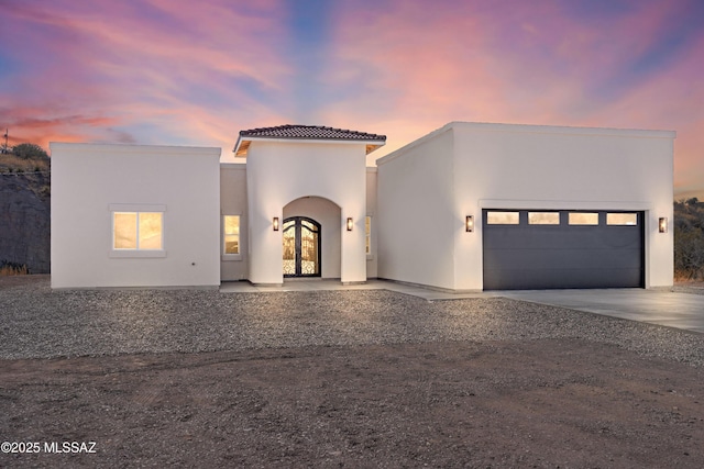 view of front of home featuring stucco siding, a garage, a tile roof, french doors, and concrete driveway