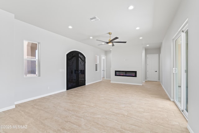unfurnished living room with a glass covered fireplace, recessed lighting, a ceiling fan, and arched walkways