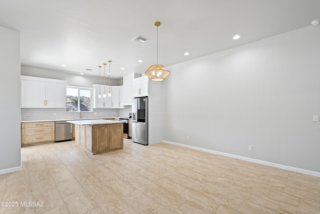 kitchen with tasteful backsplash, a kitchen island, light countertops, white cabinets, and appliances with stainless steel finishes