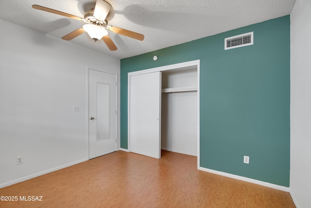 unfurnished bedroom with ceiling fan, a textured ceiling, wood finished floors, visible vents, and a closet