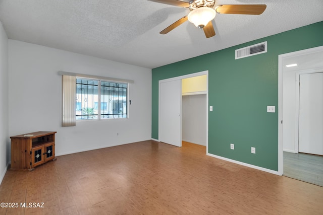 unfurnished bedroom featuring a textured ceiling, baseboards, wood finished floors, and visible vents