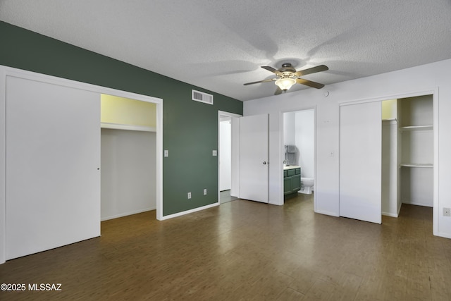 unfurnished bedroom with visible vents, baseboards, a textured ceiling, dark wood finished floors, and ensuite bath