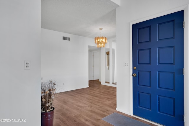 foyer with a textured ceiling, visible vents, wood finished floors, baseboards, and a chandelier