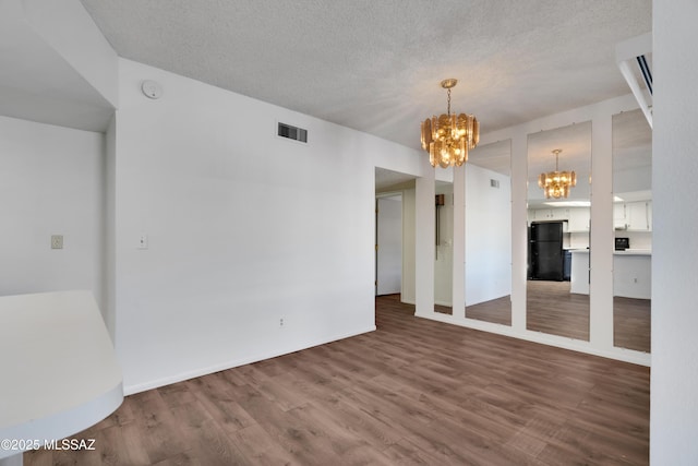 unfurnished room with baseboards, visible vents, wood finished floors, and a chandelier