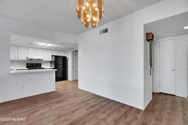 kitchen featuring light countertops, baseboards, wood finished floors, under cabinet range hood, and black appliances