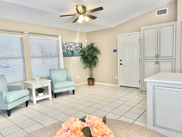 sitting room featuring vaulted ceiling, visible vents, a ceiling fan, light tile patterned flooring, and a textured ceiling