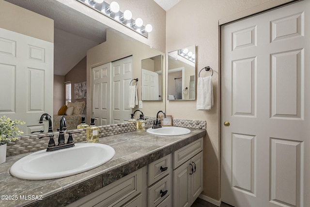 ensuite bathroom featuring double vanity, connected bathroom, lofted ceiling, and a sink