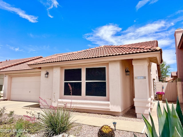 view of front of home with fence, a tiled roof, stucco siding, driveway, and a garage