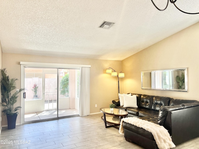 living area with lofted ceiling, a textured ceiling, visible vents, and light wood-style flooring