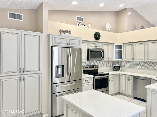 kitchen with stainless steel appliances, vaulted ceiling, visible vents, backsplash, and light countertops