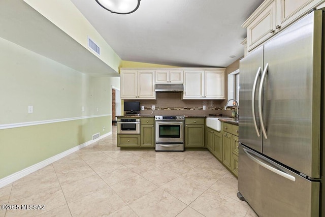 kitchen featuring decorative backsplash, lofted ceiling, dark countertops, under cabinet range hood, and appliances with stainless steel finishes