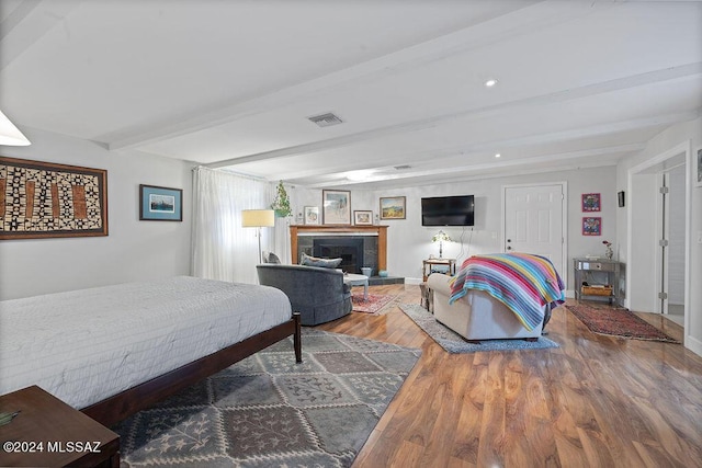 bedroom featuring a fireplace with raised hearth, recessed lighting, wood finished floors, beamed ceiling, and visible vents