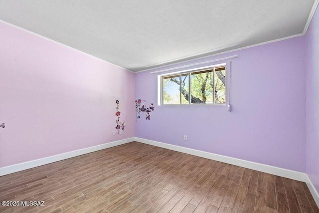 spare room featuring crown molding, baseboards, and wood finished floors