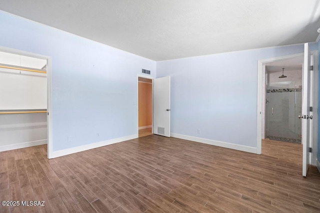 unfurnished bedroom featuring visible vents, baseboards, wood finished floors, and a spacious closet