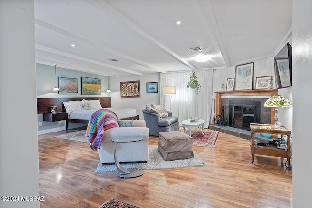 living area featuring visible vents, beam ceiling, a tile fireplace, wood finished floors, and baseboards