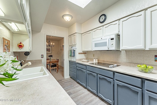kitchen with light countertops, backsplash, white appliances, and a sink