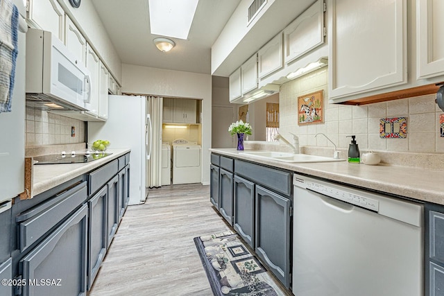 kitchen with backsplash, a skylight, a sink, white appliances, and washer and clothes dryer