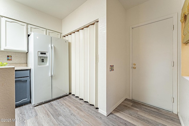 kitchen with light countertops, decorative backsplash, white refrigerator with ice dispenser, and light wood-type flooring