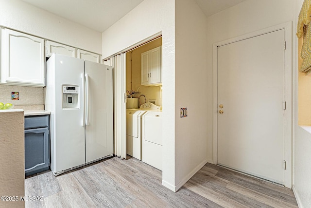 kitchen with decorative backsplash, white refrigerator with ice dispenser, light countertops, light wood-style flooring, and washer and clothes dryer