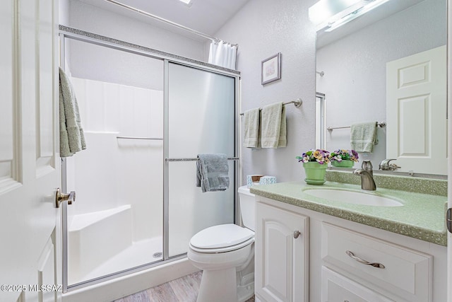 full bath featuring vanity, a shower stall, toilet, and wood finished floors