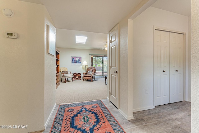 hallway featuring a textured wall, baseboards, and light wood-style floors