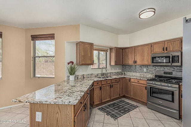 kitchen with brown cabinetry, a sink, light tile patterned floors, a peninsula, and stainless steel appliances