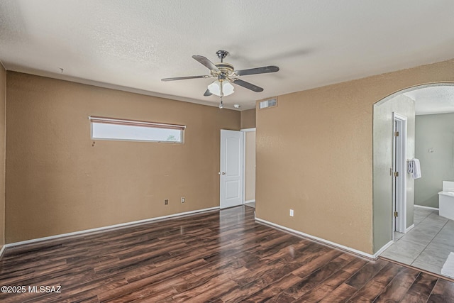 unfurnished bedroom featuring visible vents, arched walkways, wood finished floors, baseboards, and ensuite bathroom