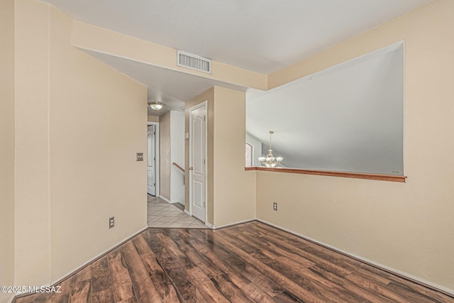 unfurnished room featuring baseboards, visible vents, wood finished floors, and an inviting chandelier