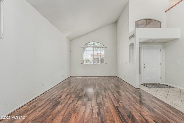unfurnished living room with visible vents, baseboards, wood finished floors, and high vaulted ceiling