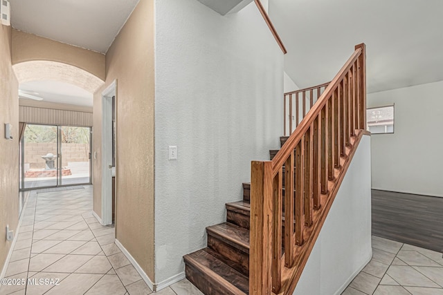 stairs with arched walkways, a textured wall, and tile patterned floors