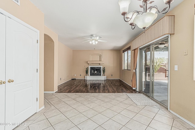 unfurnished living room featuring visible vents, light tile patterned flooring, baseboards, a fireplace with raised hearth, and ceiling fan with notable chandelier