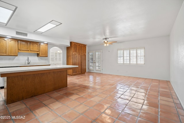 kitchen with visible vents, a ceiling fan, a kitchen island, light countertops, and a sink
