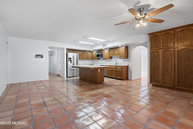 kitchen with a center island, arched walkways, a sink, light countertops, and stainless steel appliances
