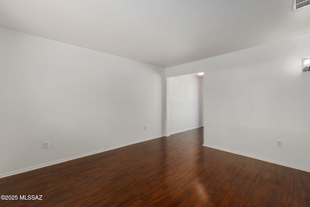 spare room with dark wood-style floors, visible vents, and baseboards