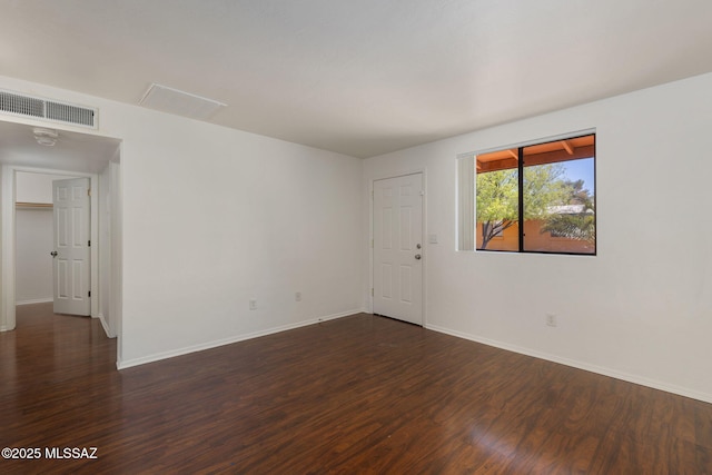 spare room with baseboards, visible vents, and dark wood-style flooring