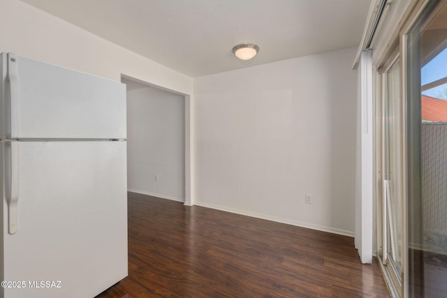 unfurnished bedroom with baseboards, freestanding refrigerator, and dark wood finished floors