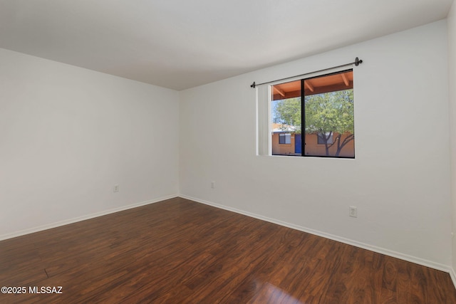 spare room with baseboards and dark wood-style flooring