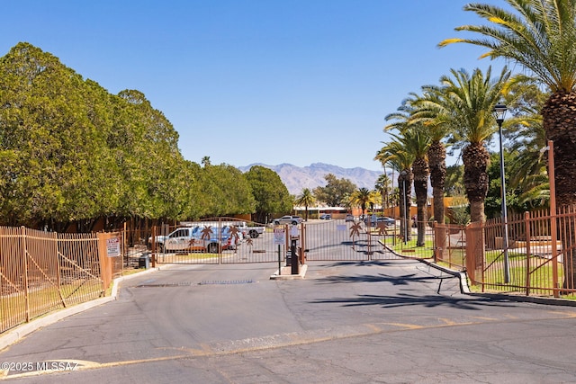 view of road featuring a gated entry, a gate, curbs, a mountain view, and street lights
