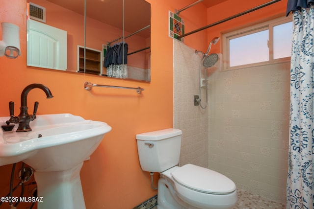full bathroom featuring a sink, toilet, tiled shower, and visible vents