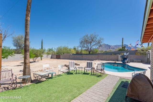 view of swimming pool featuring a fenced backyard, a water slide, a fenced in pool, a mountain view, and a storage shed