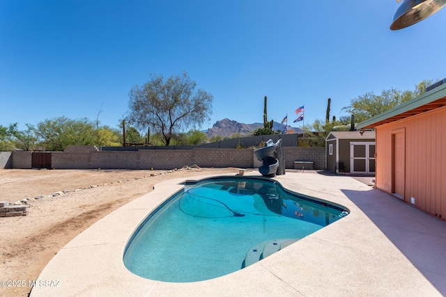 view of pool with a patio, a fenced backyard, a storage shed, a water slide, and an outbuilding