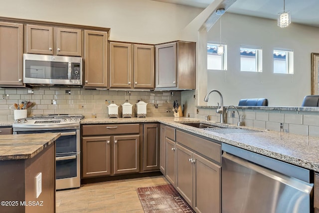 kitchen featuring decorative light fixtures, tasteful backsplash, a sink, stainless steel appliances, and light wood-style flooring