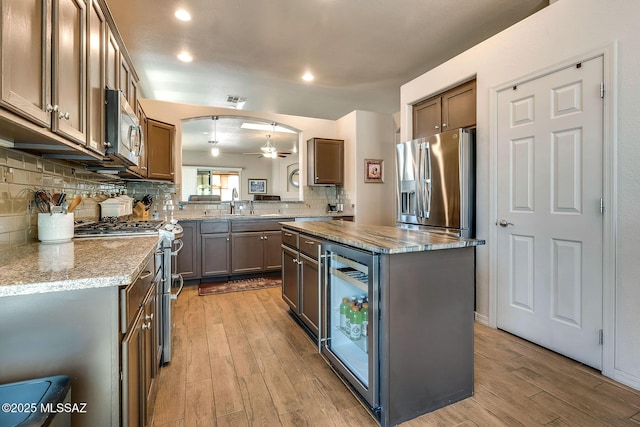 kitchen featuring appliances with stainless steel finishes, light wood-style flooring, wine cooler, backsplash, and a kitchen island