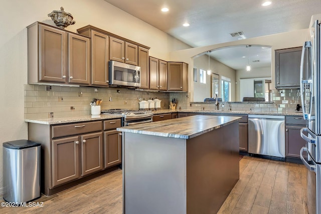kitchen with light wood-style floors, a sink, decorative backsplash, and appliances with stainless steel finishes