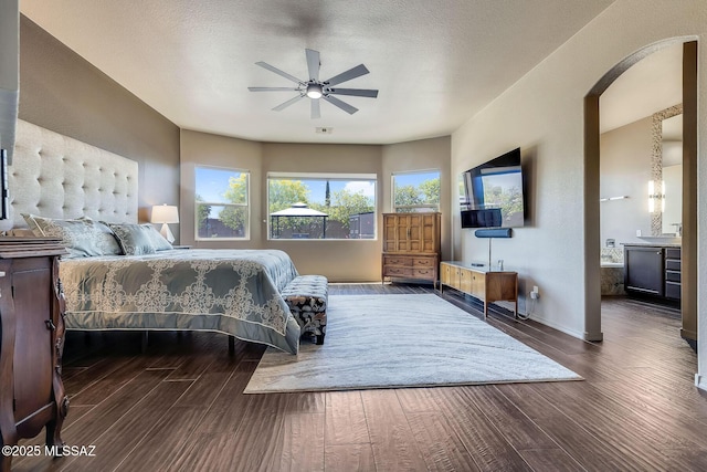 bedroom featuring baseboards, arched walkways, wood finished floors, and connected bathroom