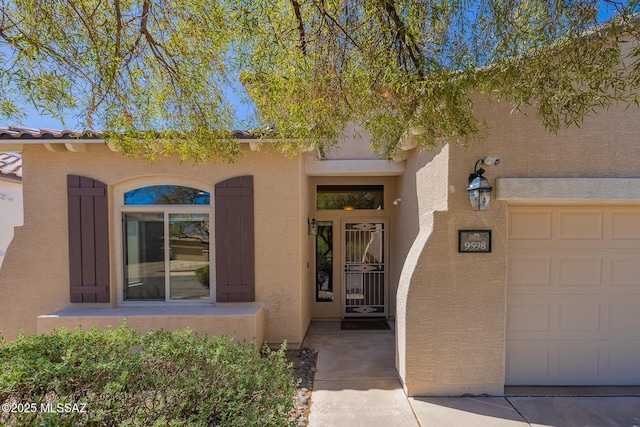 view of exterior entry with a garage and stucco siding