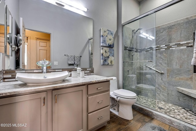 bathroom featuring vanity, a stall shower, toilet, and wood finished floors
