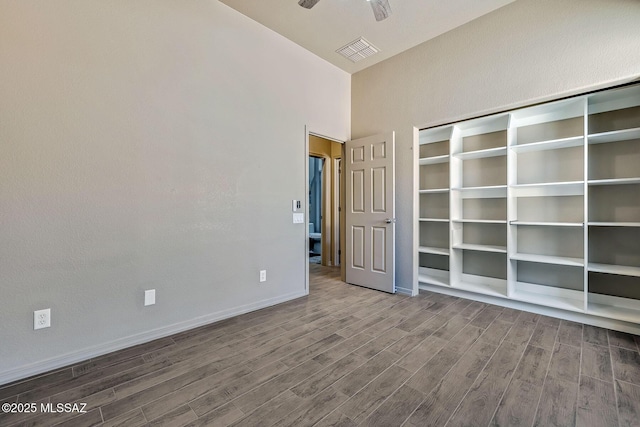 spare room with ceiling fan, visible vents, wood finished floors, baseboards, and a high ceiling